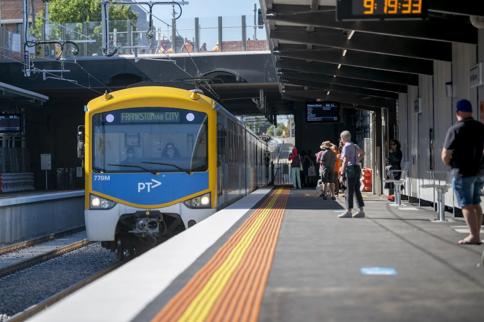 Passenger train arriving at a newly upgraded station platform, with commuters waiting under the canopy and accessible platform markings in the foreground.