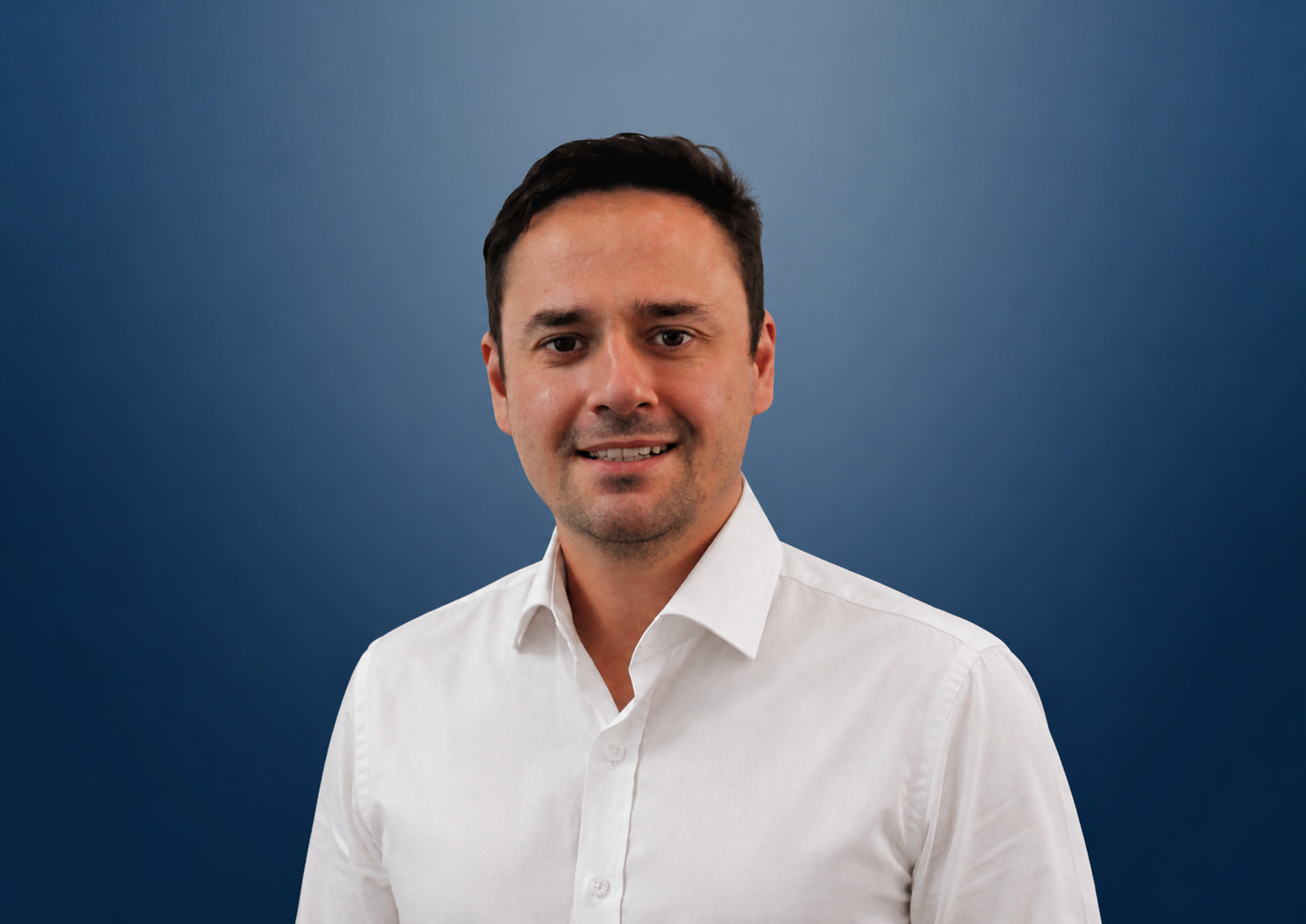 A young man, Chris Zagami, in a navy blue suit and white dress shirt, smiling, posed against a gradient blue background.