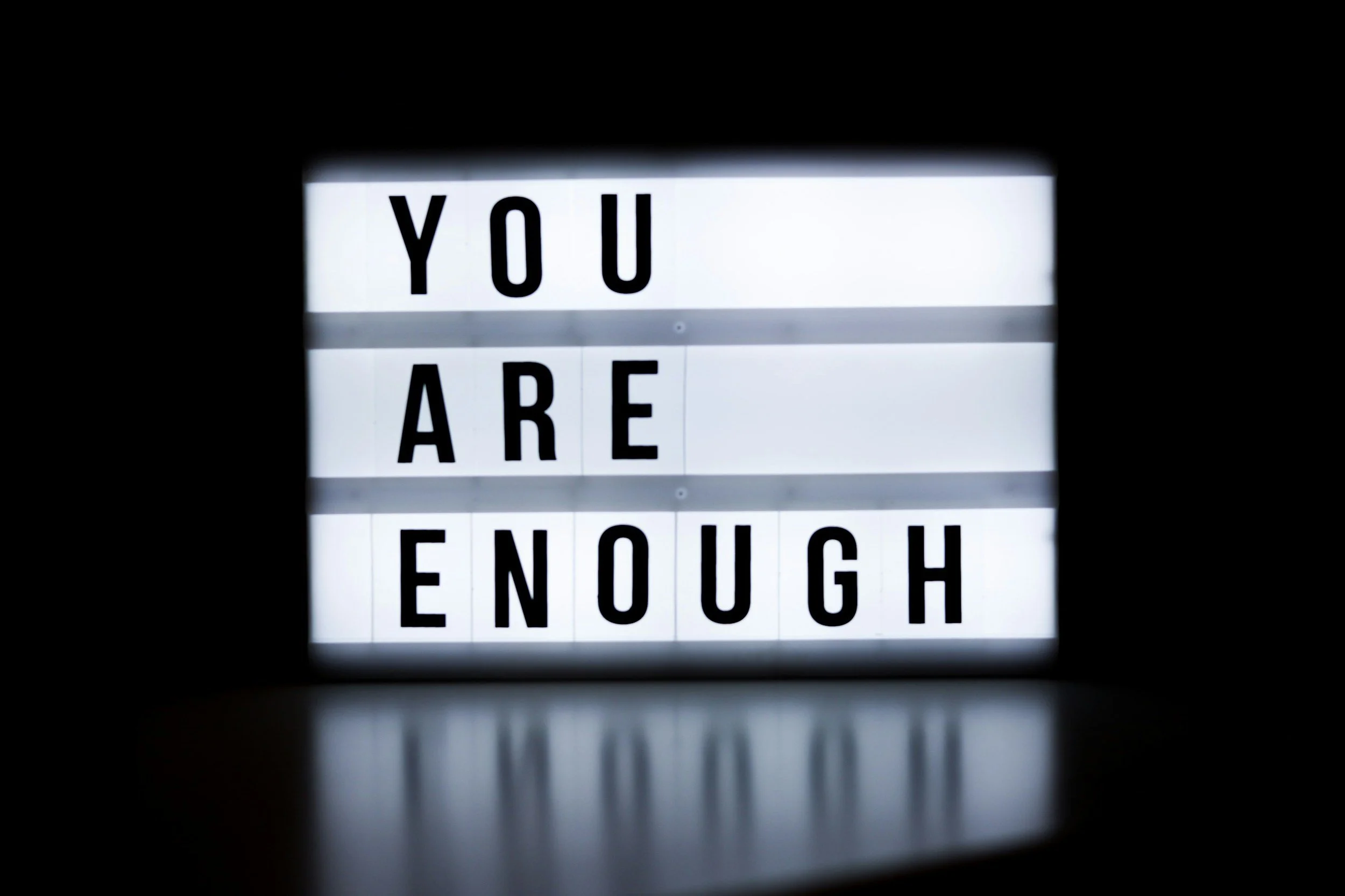 Illuminated sign with the message 'You Are Enough' in bold black letters on white background