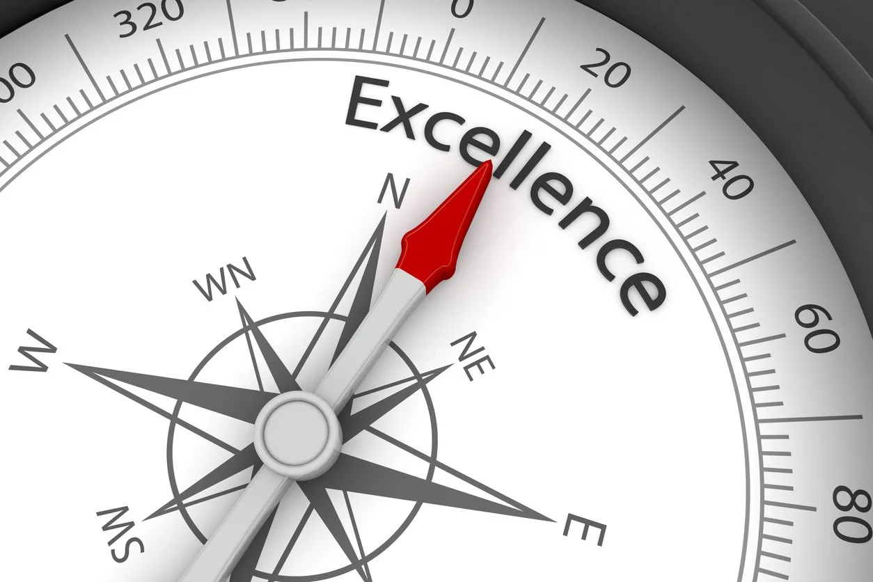 A compass with a red needle pointing to the word "Excellence" on a circular dial, indicating the direction of excellence.