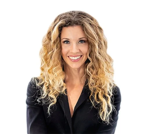 Woman with curly blonde hair smiling, wearing a black blazer, against a white background.