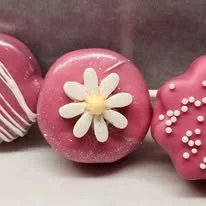 Pink cake pops decorated with white and yellow fondant flowers and pink icing with white sprinkles.