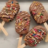 Four chocolate-covered ice cream bars with colorful sprinkles on top, on a wooden tray.