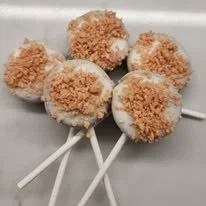 Four marshmallow pops coated in crushed graham crackers on white sticks