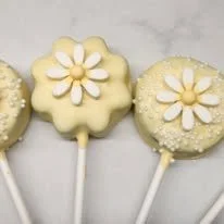 Three yellow cake pops decorated with white flower designs on sticks