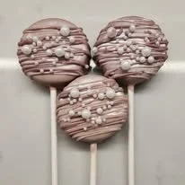 Three pink cake pops decorated with small white and pink candies on white sticks.