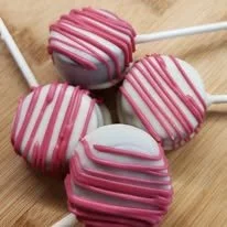 Four pink and white striped cake pops on a wooden surface.