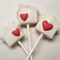 Three square marshmallow lollipops with red heart decorations, placed on a light background.