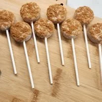 Six chocolate cake pops on sticks arranged on a wooden surface.