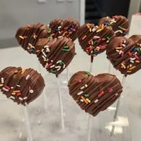 Heart-shaped chocolate cake pops decorated with colorful sprinkles on sticks