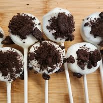 Seven cake pops coated in white chocolate with crushed cookie topping on wooden sticks.