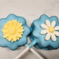 Two lollipops with flower-shaped tops, one with a yellow flower and one with a white flower, and blue wrappers.