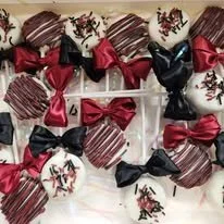 Assorted decorated chocolates wrapped in red and black ribbons arranged on a white surface.