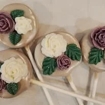 Lollipops decorated with edible flowers and leaves, resembling roses and greenery.