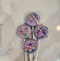 Five purple spoons with sprinkles on top, arranged on a marble surface