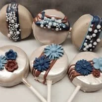 A display of decorated cake pops with blue, brown, and black floral designs and white and dark chocolate coatings.