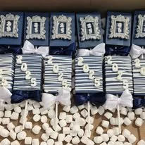 Decorative blue and white-themed birthday setup with letters spelling 'HAPPY BIRTHDAY', wrapped gifts or favors, and marshmallows or sugar cubes at the bottom.