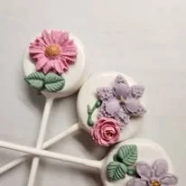 Decorative lollipops with floral and animal designs, featuring pink, purple, and white flowers with green leaves.