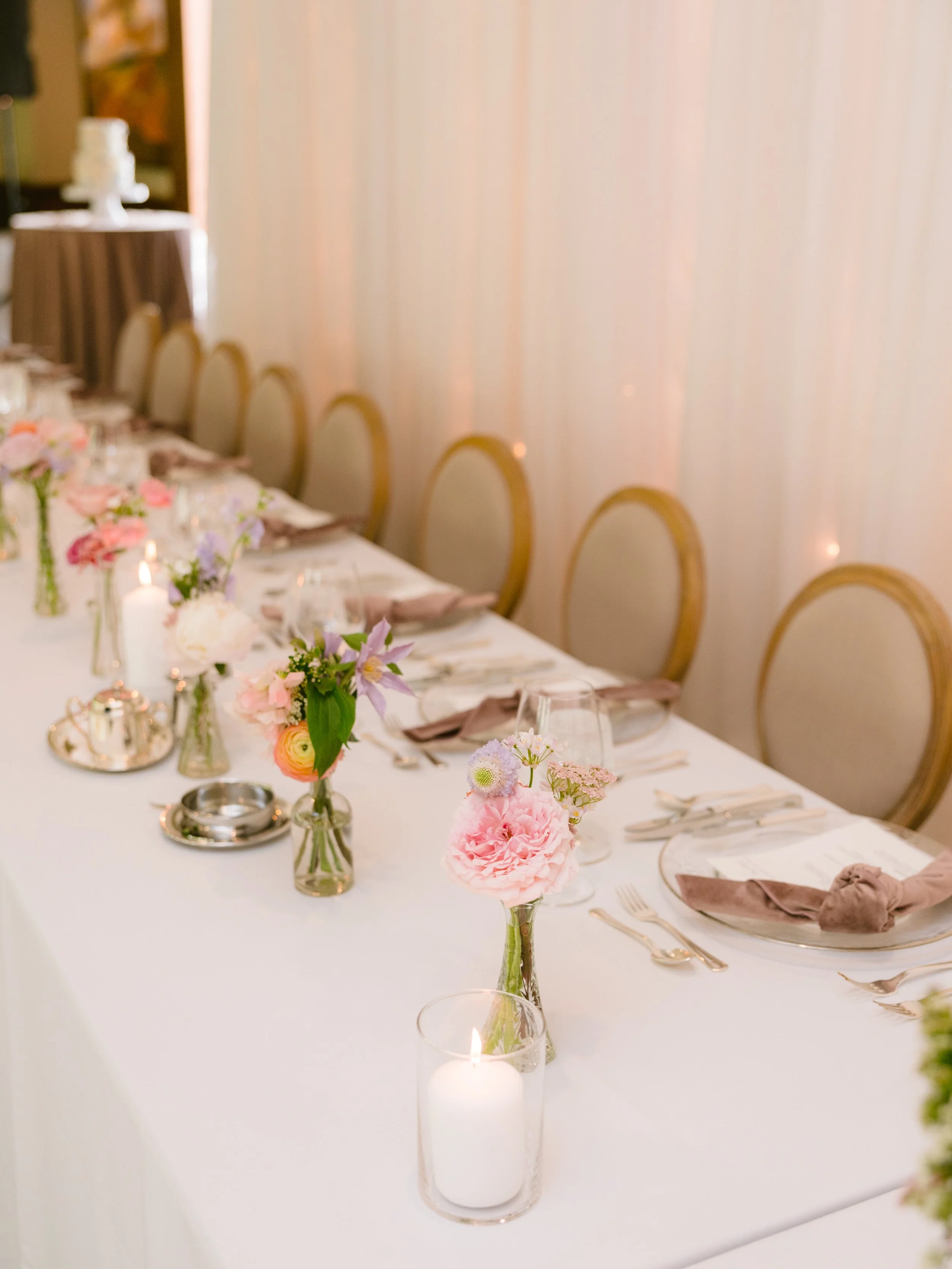 Elegant dining table decorated with pink and purple floral centerpieces, candles, and neatly arranged tableware for a formal event.