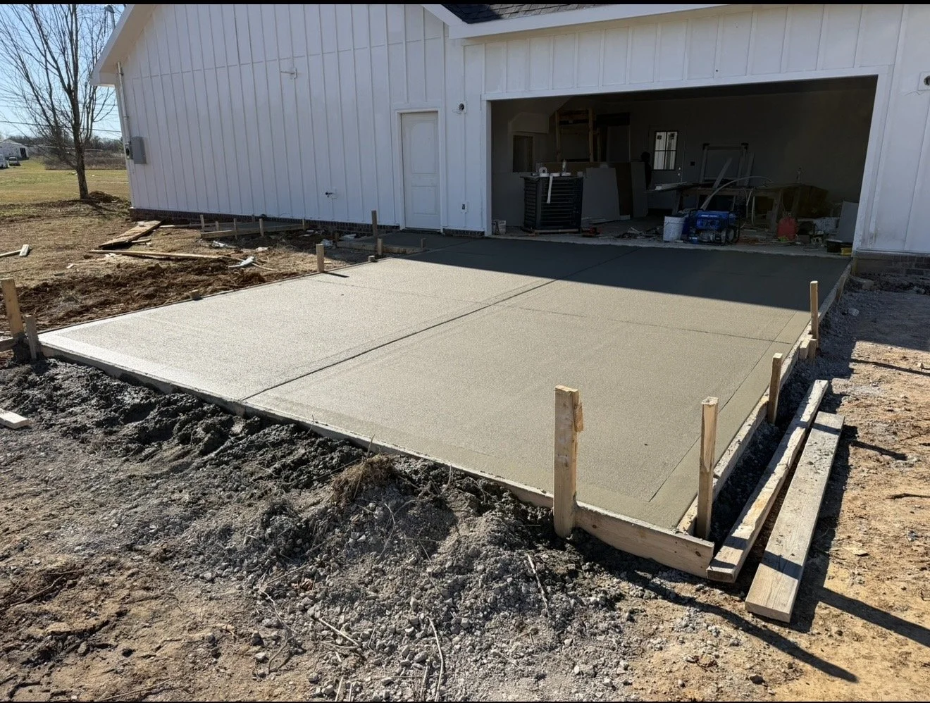 Freshly poured concrete slab for a garage foundation in front of a white building under construction.
