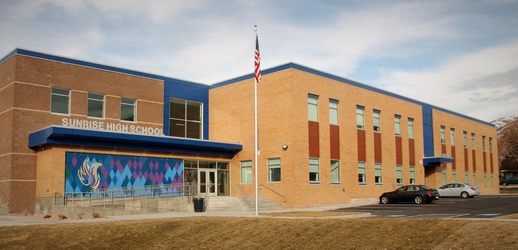 The exterior of Sunrise High School, a modern brick school building with blue accents, a large sign, and an American flag in front.