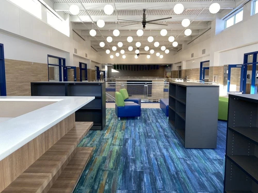 Empty indoor space with high ceiling, white walls, modern lighting, and colorful seating, possibly a lounge or communal area in a public building.