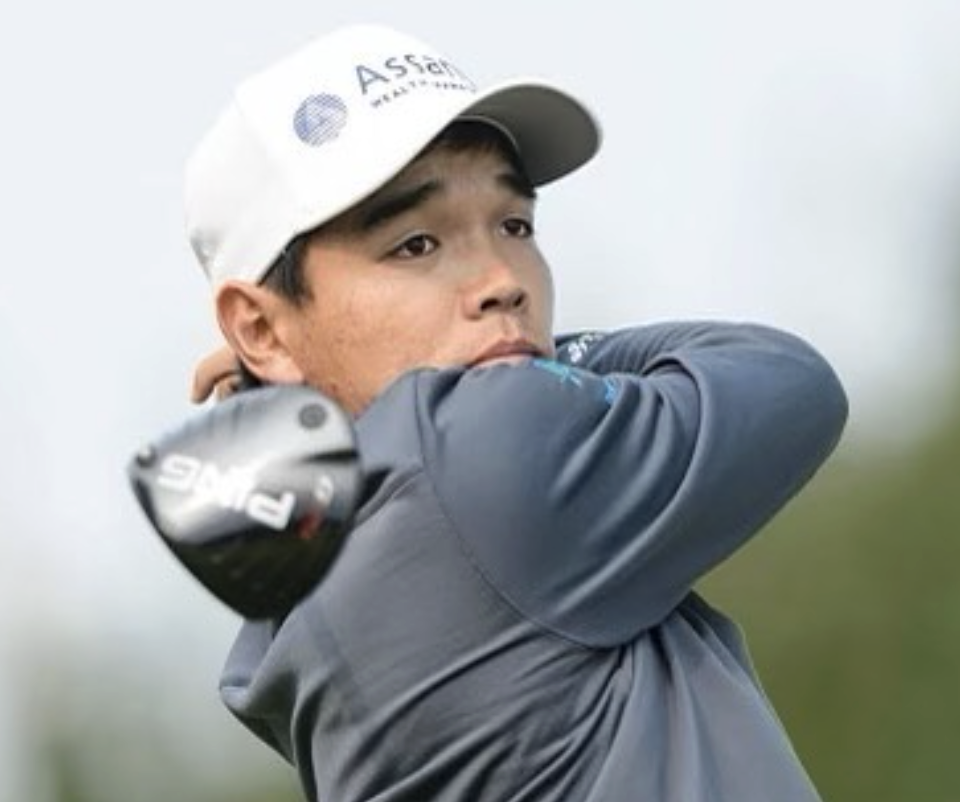 A modern house sits on a grassy hill in a mountainous landscape with snow-capped peaks in the distance and cloudy sky overhead.