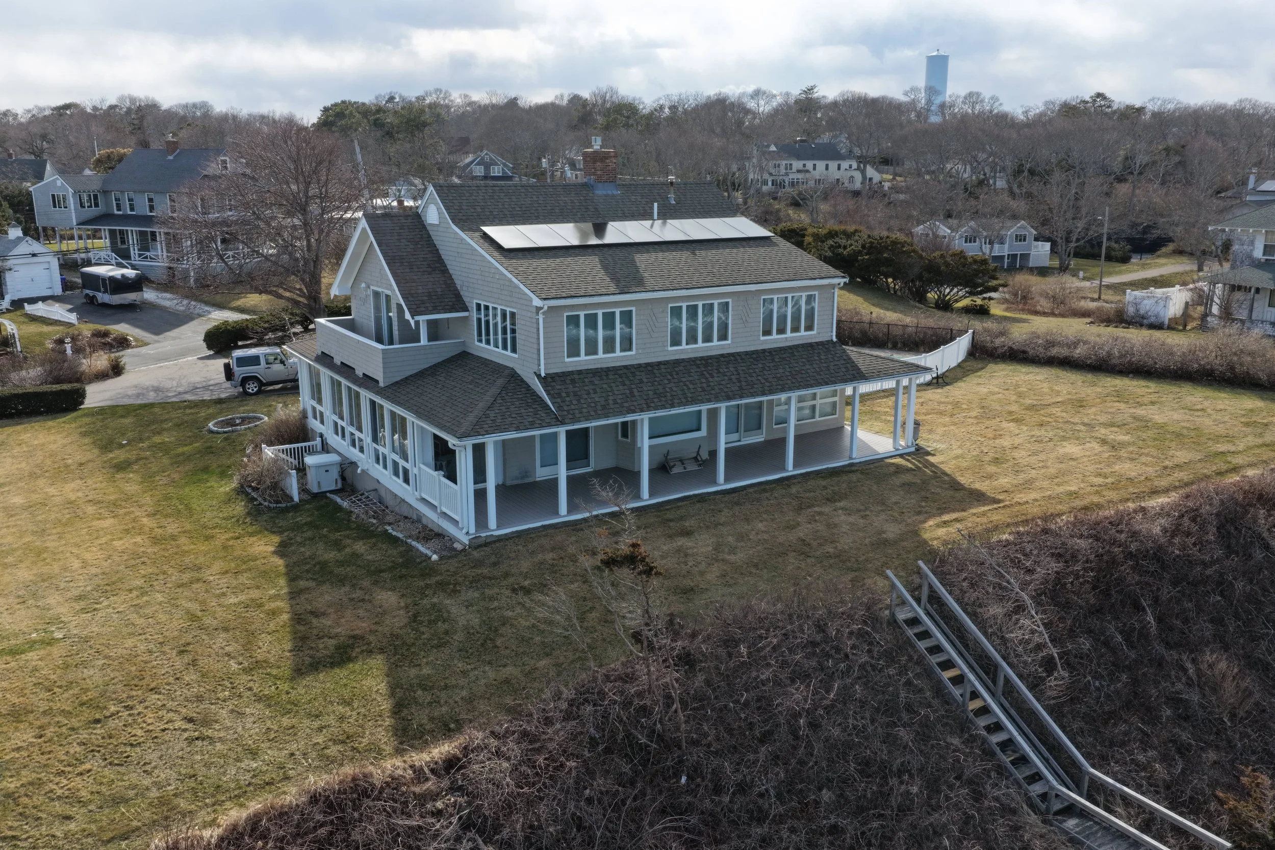 A large two-story house with a spacious backyard, solar panels on the roof, and a wooden deck around the house, in a suburban neighborhood.