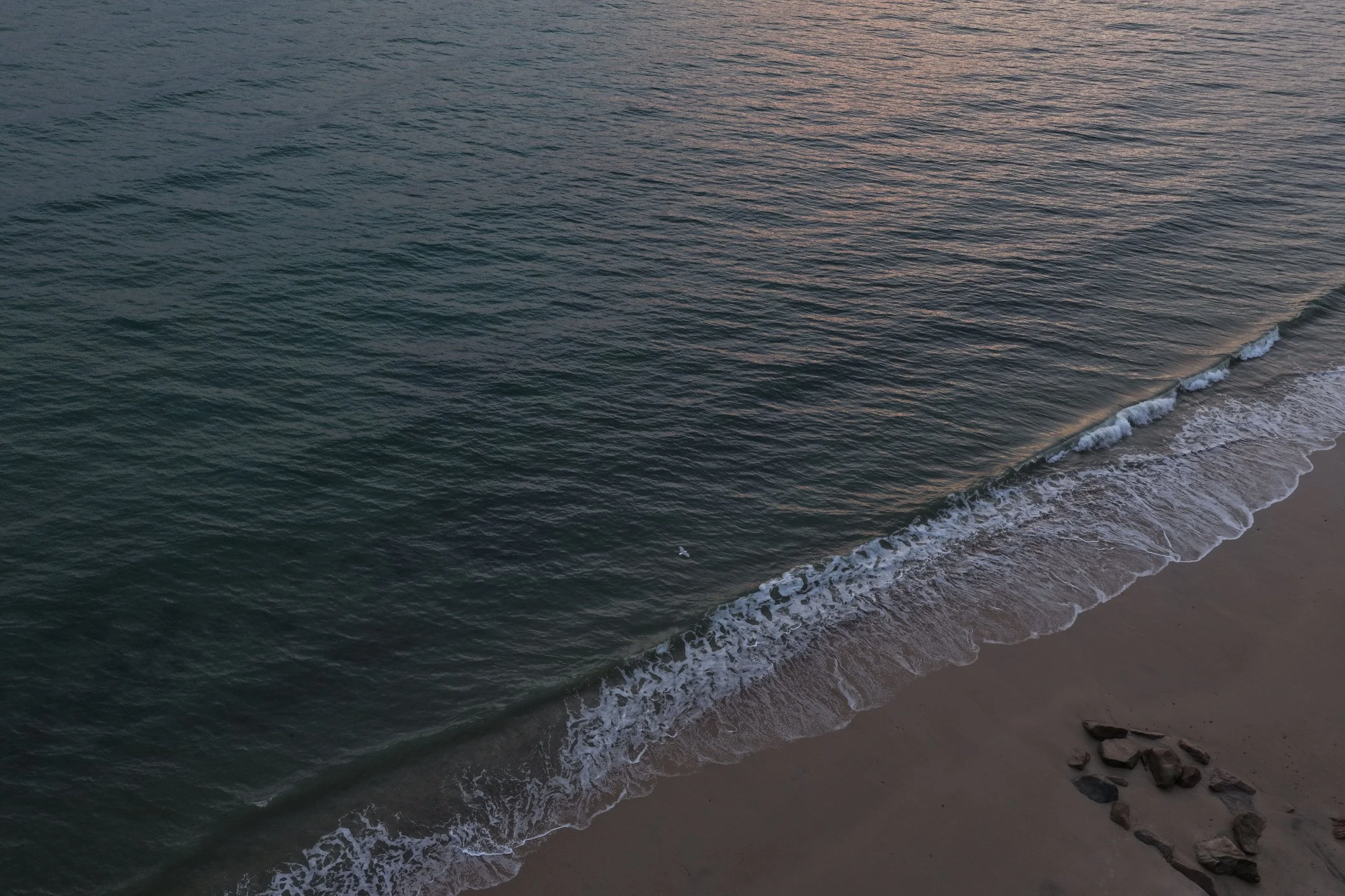 Aerial view of a beach with gentle waves and a heart shape made of rocks in the sand.