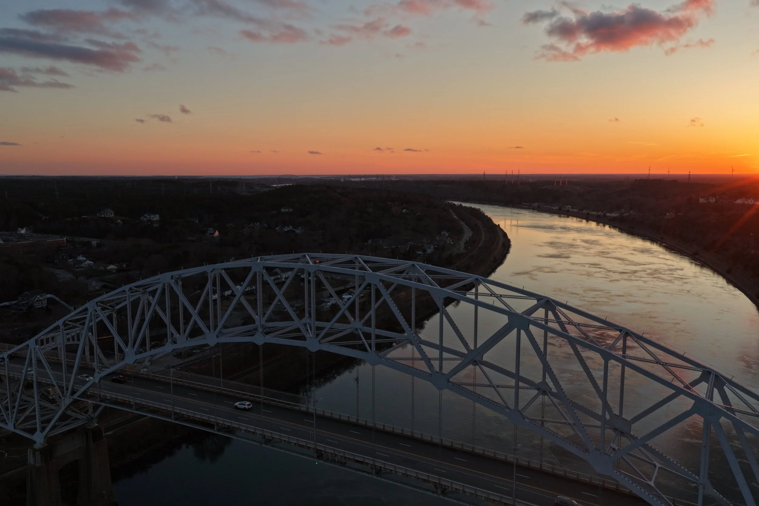 Aerial view of a bridge over a winding river at sunset with a colorful sky.