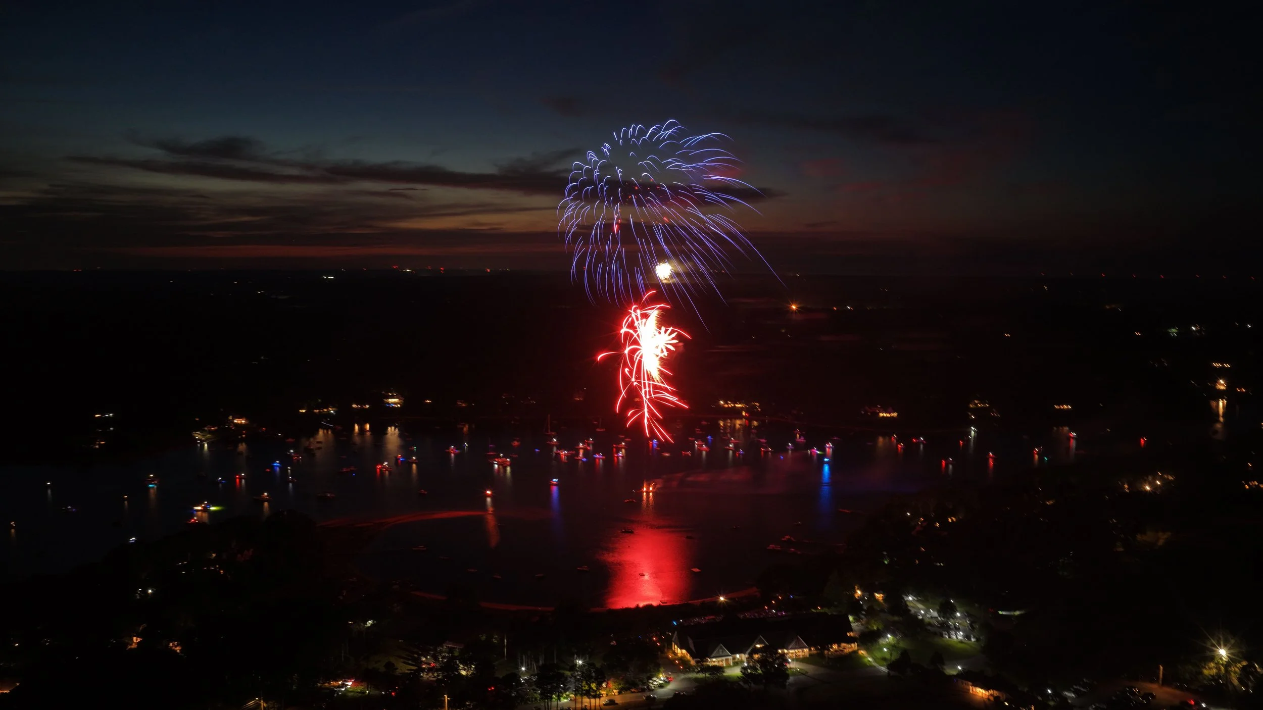 Fireworks display over a cityscape at night with reflections on the water.
