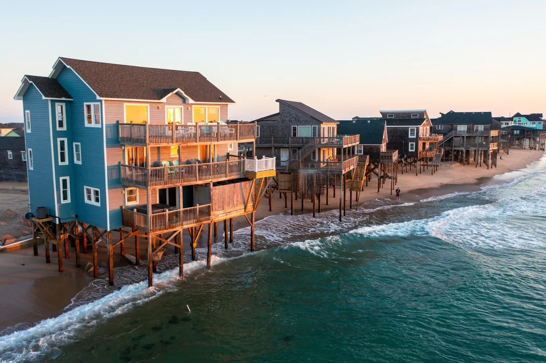 Beach houses built on stilts along the shoreline at sunset.
