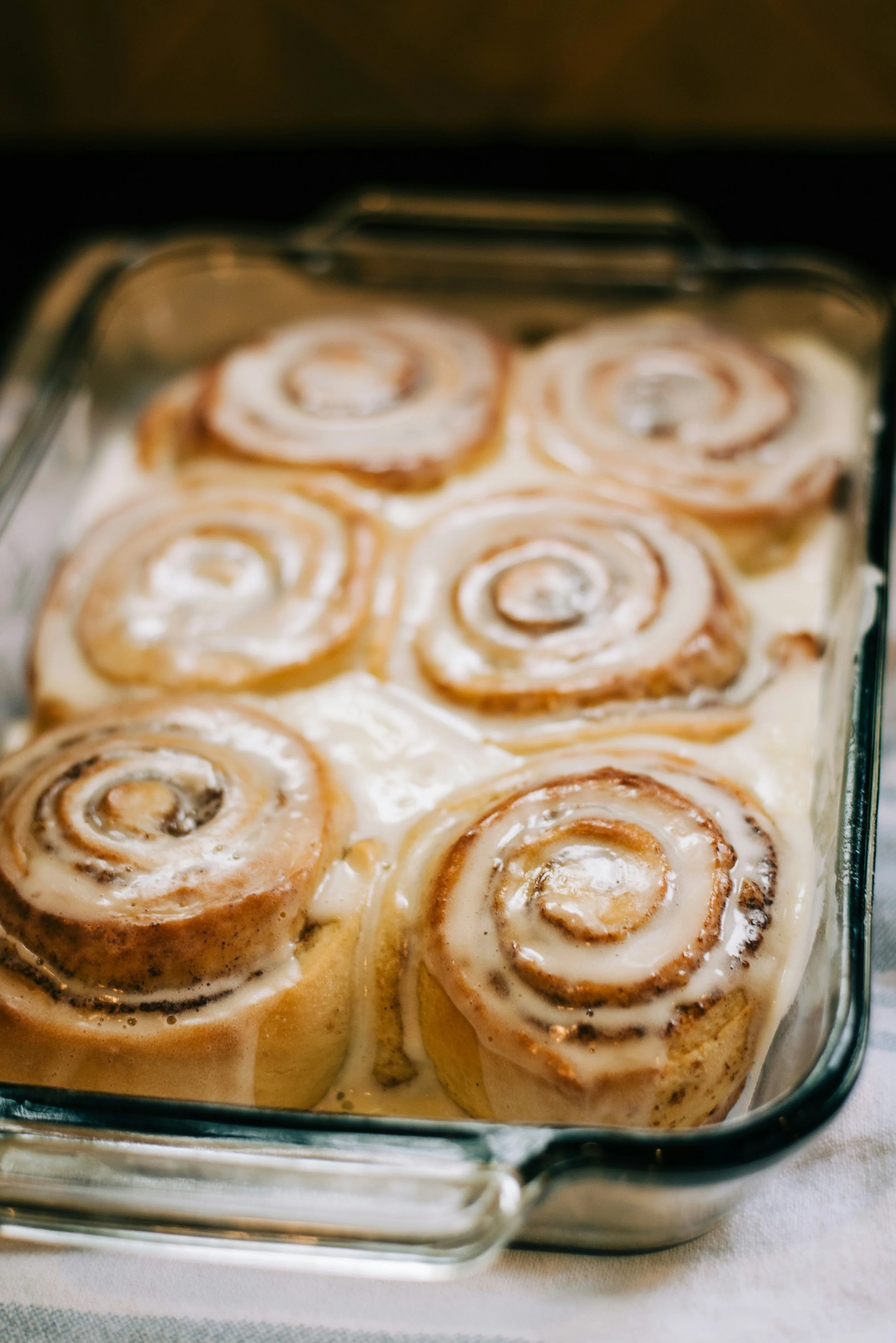 Baked cinnamon rolls topped with icing in a glass baking dish.