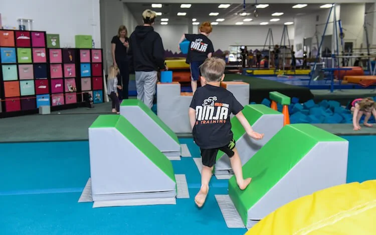 Child climbing a green and gray foam obstacle in a children's indoor gym.