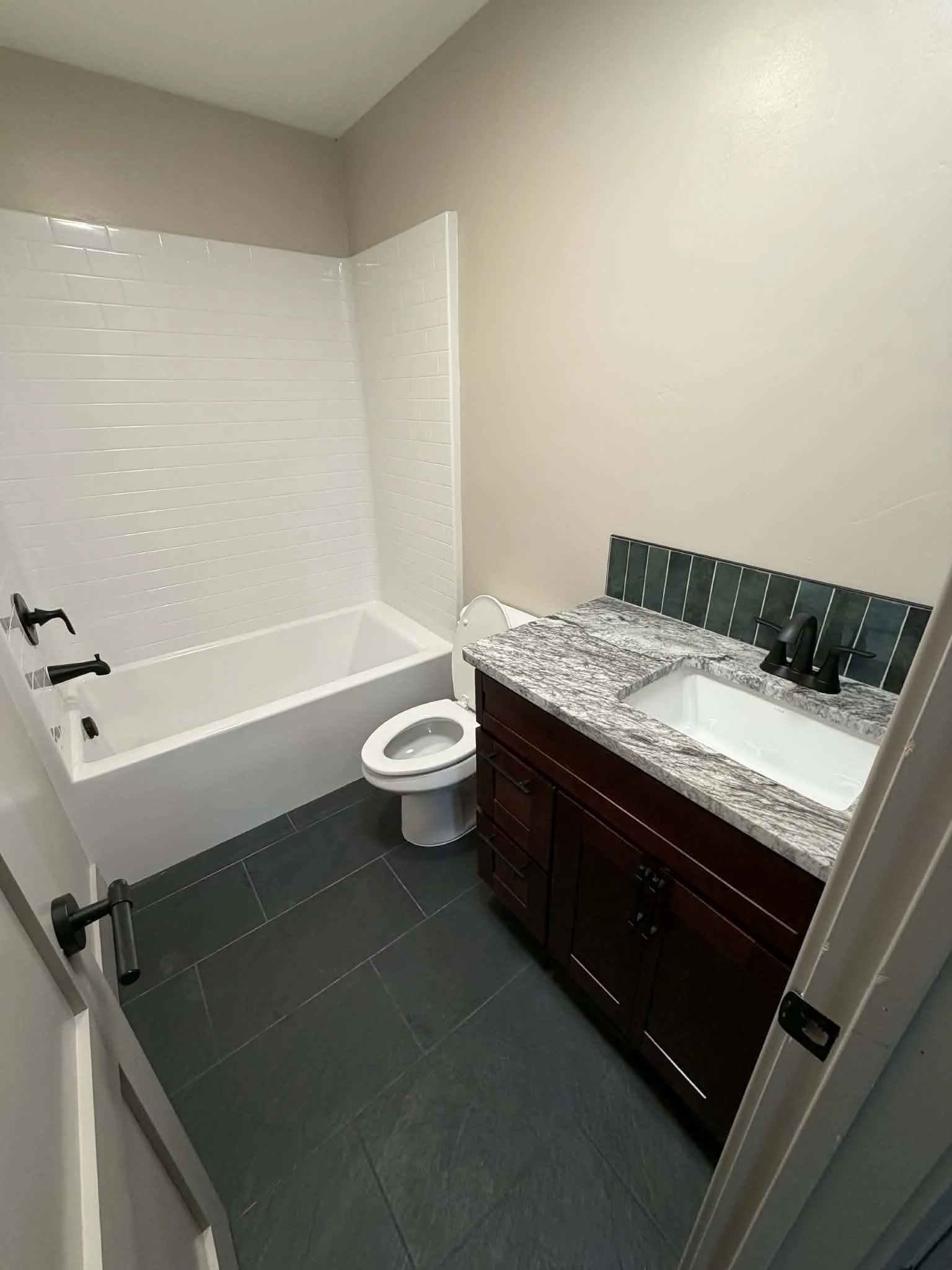 A small bathroom with a bathtub and shower, a toilet, and a vanity with a granite countertop and a rectangular sink, in a neutral color scheme.