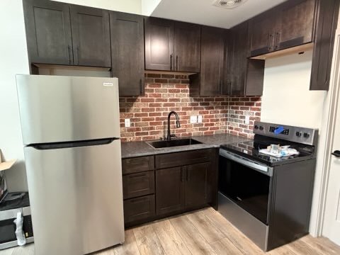 Kitchen with dark wood cabinets, brick backsplash, stainless steel refrigerator, and black stove in a modern space.