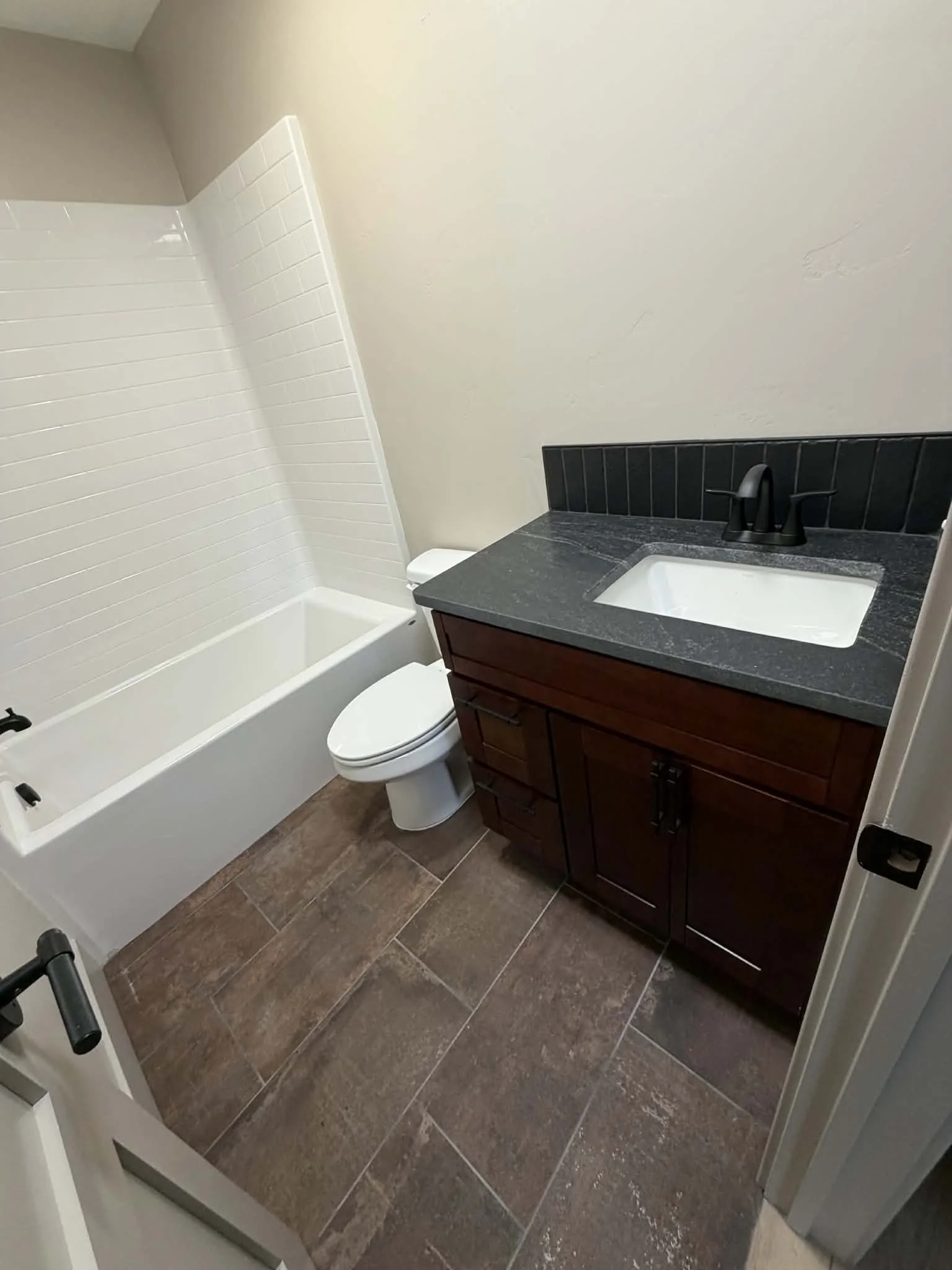 Small bathroom with a bathtub, toilet, and vanity with a black countertop and sink.