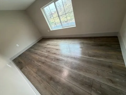Empty room with hardwood flooring and a large window offering a view outside.