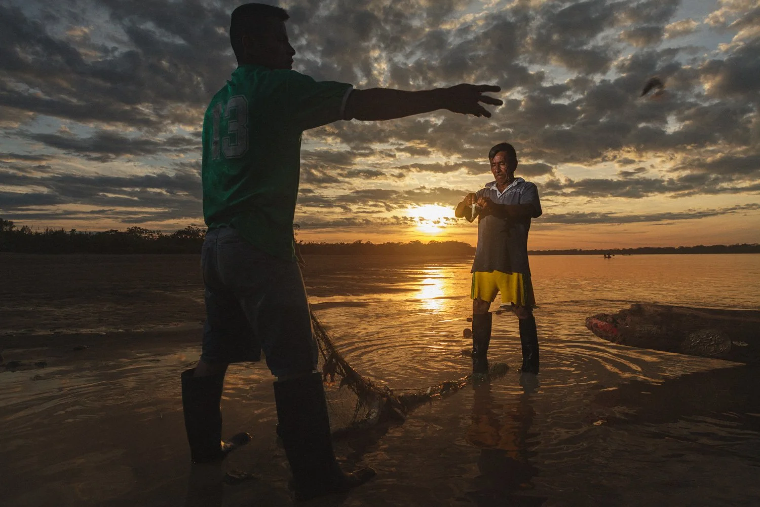 Two fishermen pulling fish from a net at sunrise on the Amazon River.