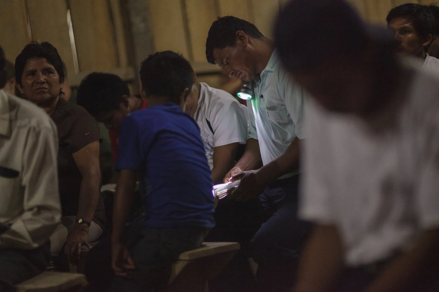 A man uses a flashlight to read his Bible during a church service in the Amazon. Most of the men spent their days outdoors from sunrise to sunset, their eyes showing the strain of years under the harsh sun.