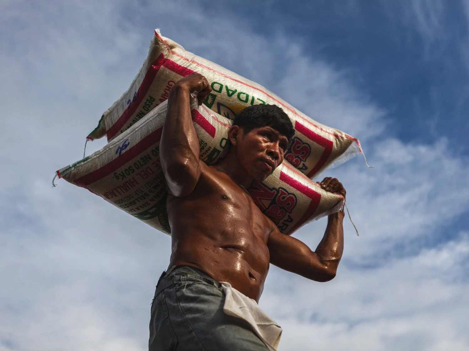 A worker in Iquitos, Peru, carries heavy bags of rice to load onto a truck. Imports like rice are vital to sustaining this isolated Amazonian city, which relies on river and air transport due to its lack of road access.