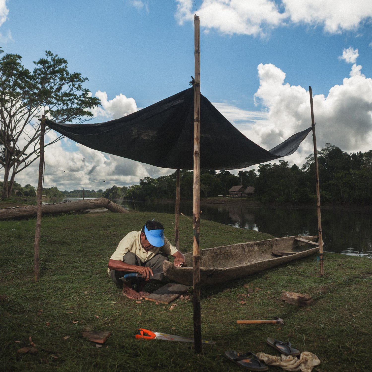A villager works by hand to shape a canoe along the Amazon River, essential for fishing and transporting goods.