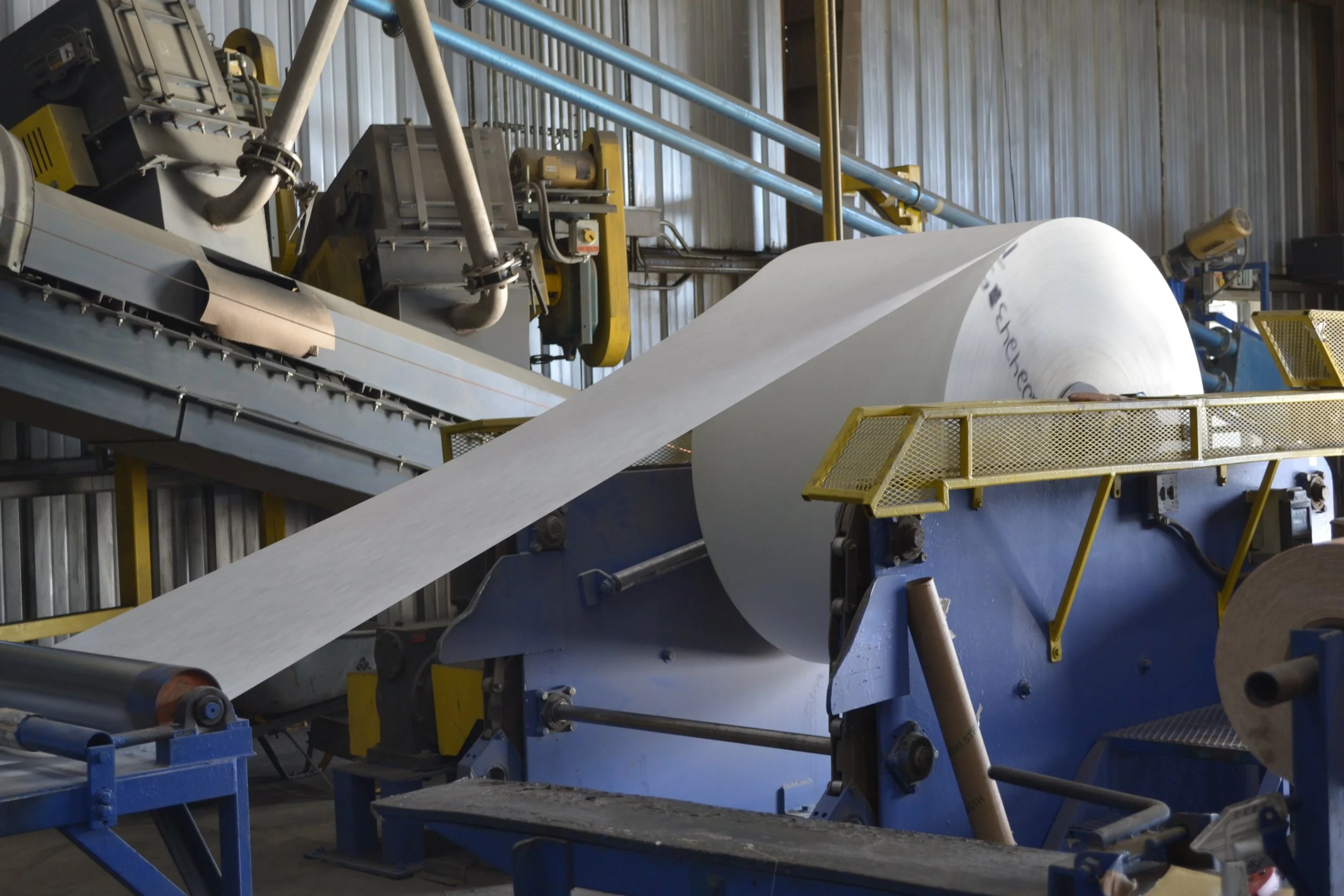 Industrial paper manufacturing machine with a large roll of paper feeding into it.