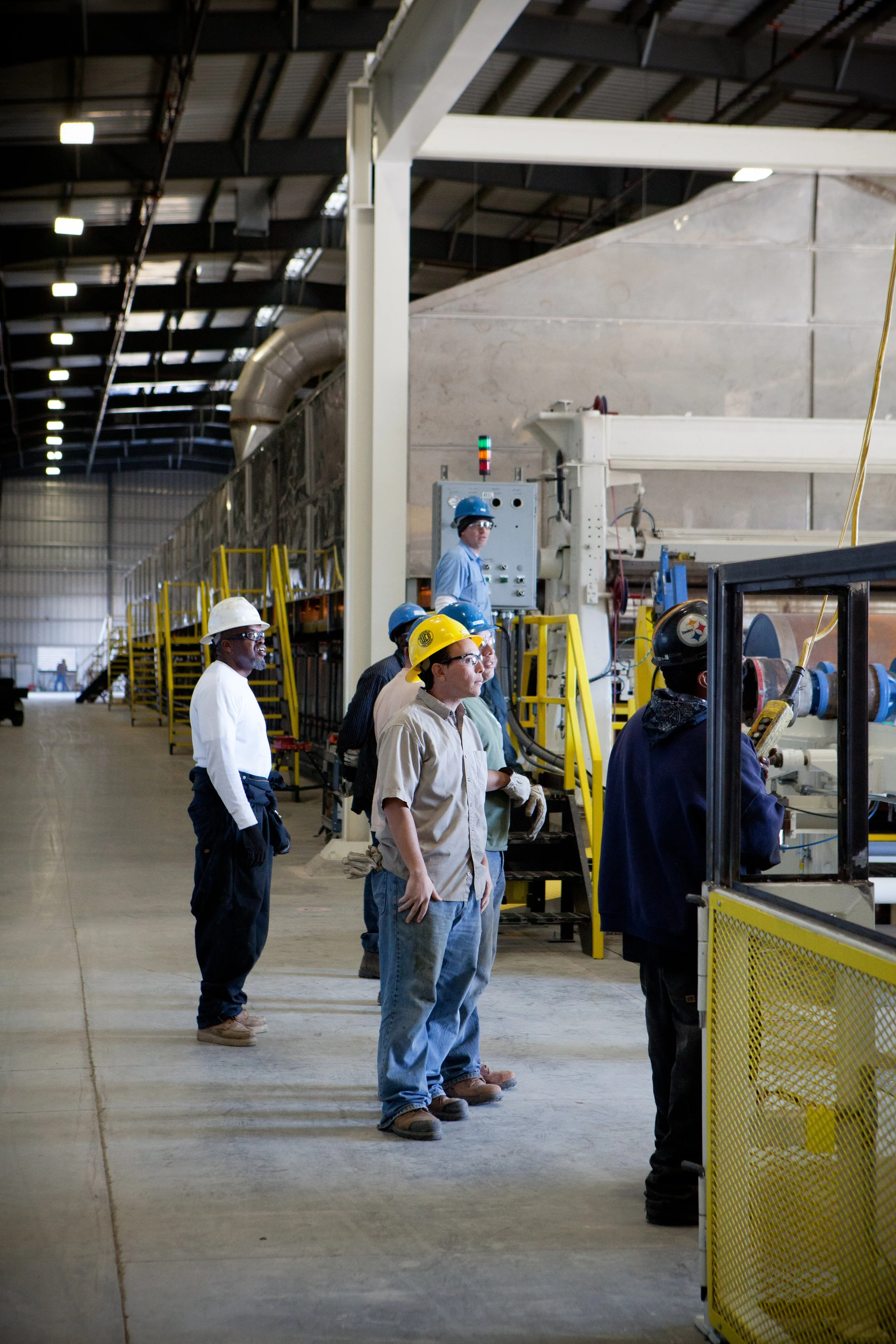 Workers wearing safety helmets inside an industrial manufacturing facility, observing machinery in operation.