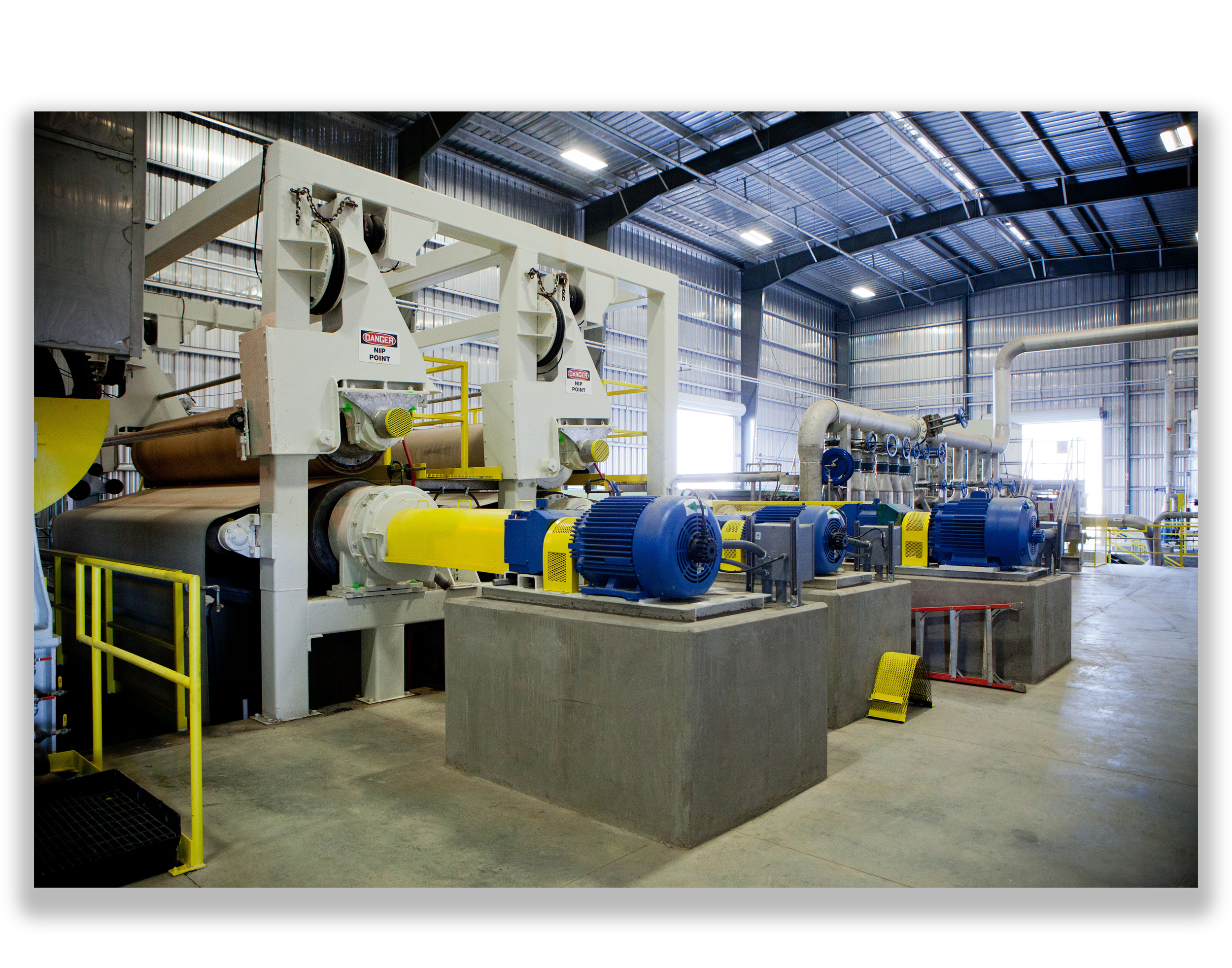 Industrial facility machinery with large blue motors and piping inside a warehouse