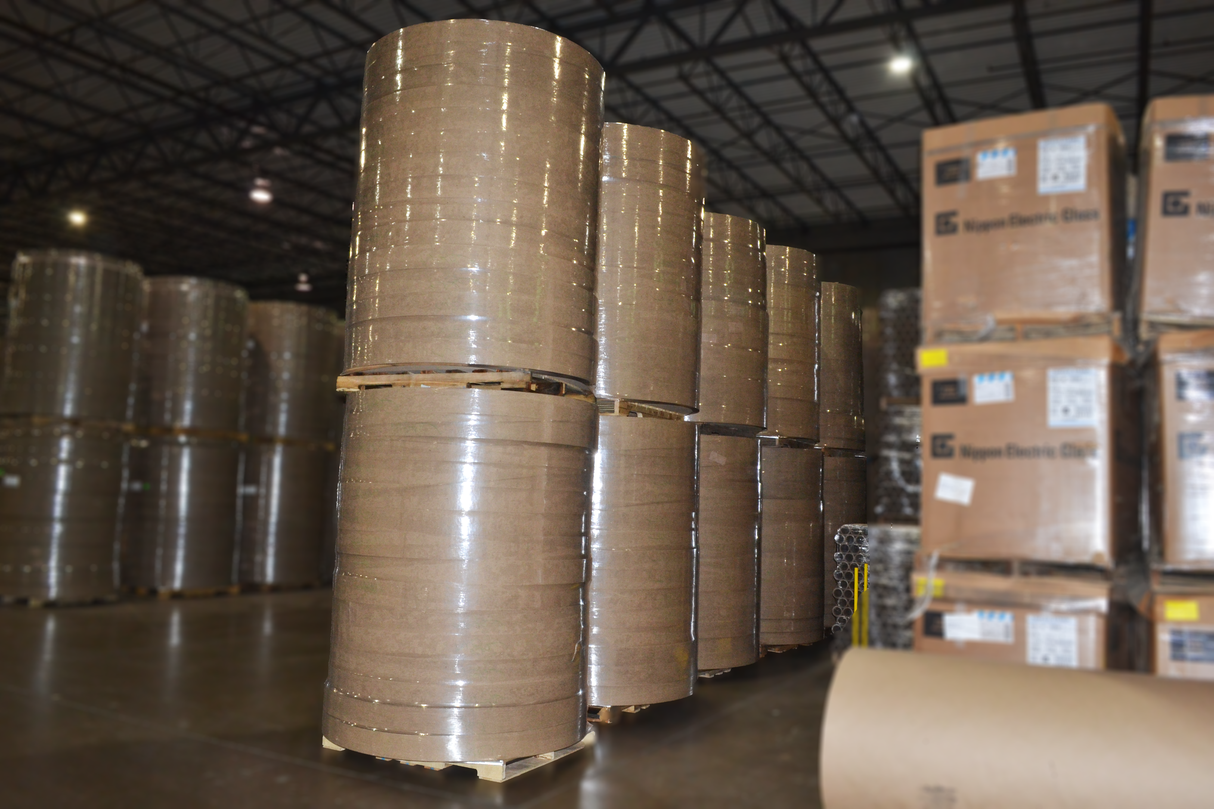 Large rolls of brown packing tape stacked in a warehouse.