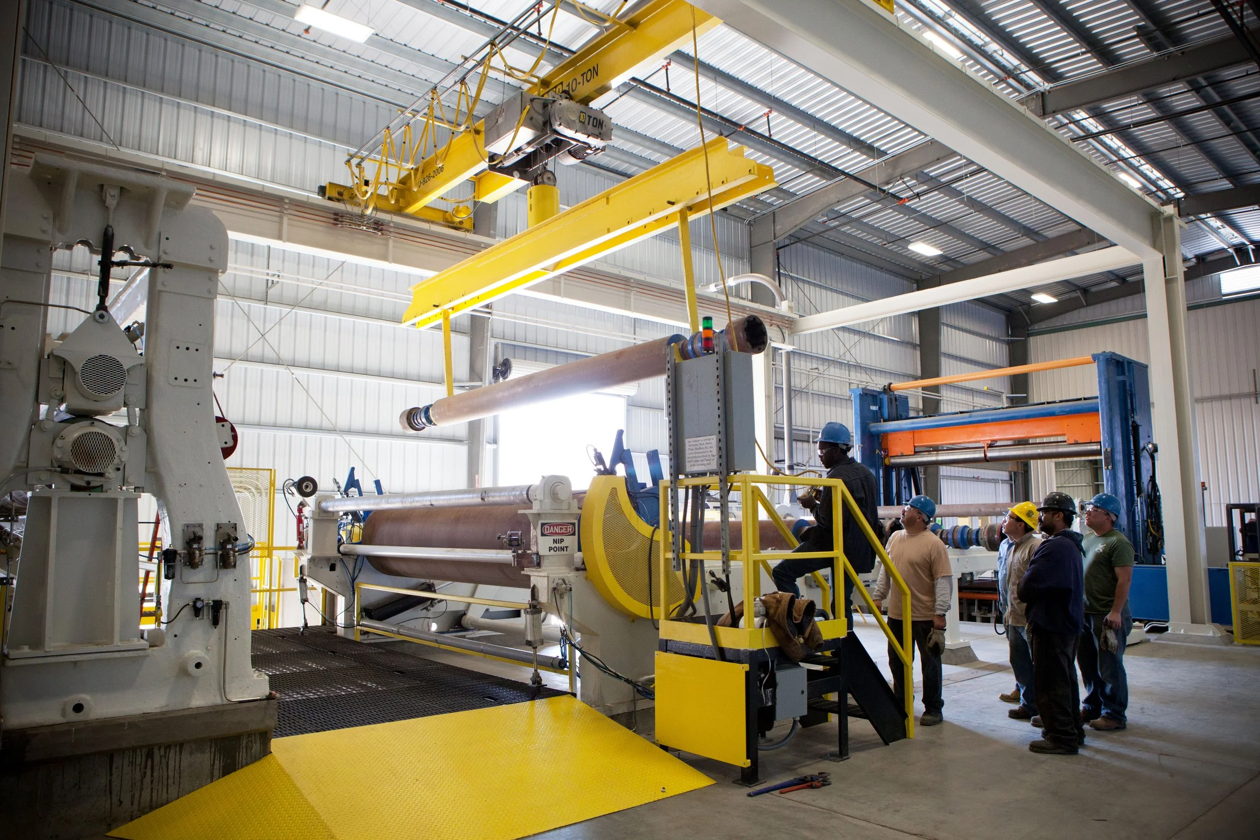 Workers in safety gear operating large industrial manufacturing equipment inside a factory.