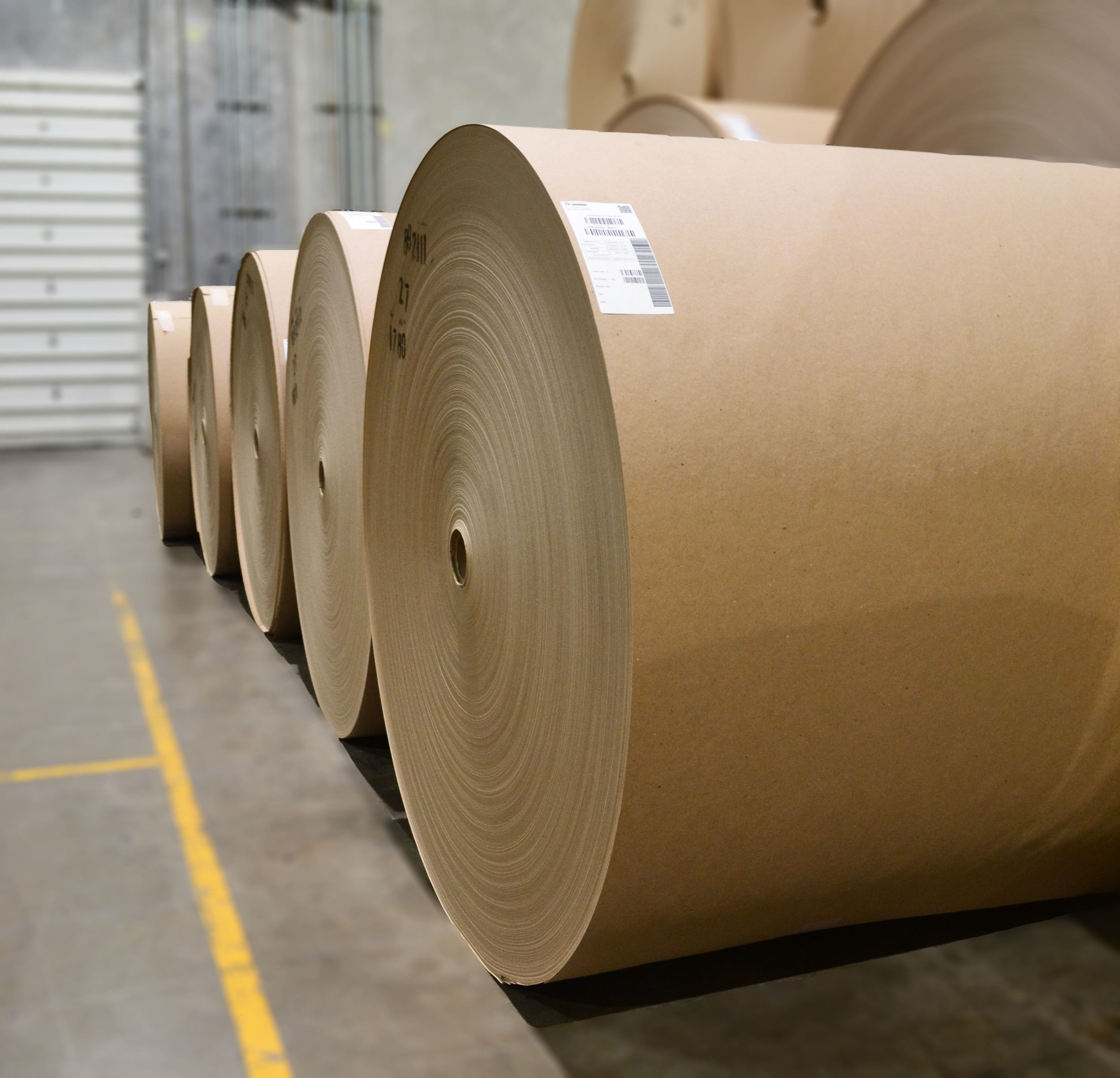 Large rolls of brown kraft paper in a warehouse.
