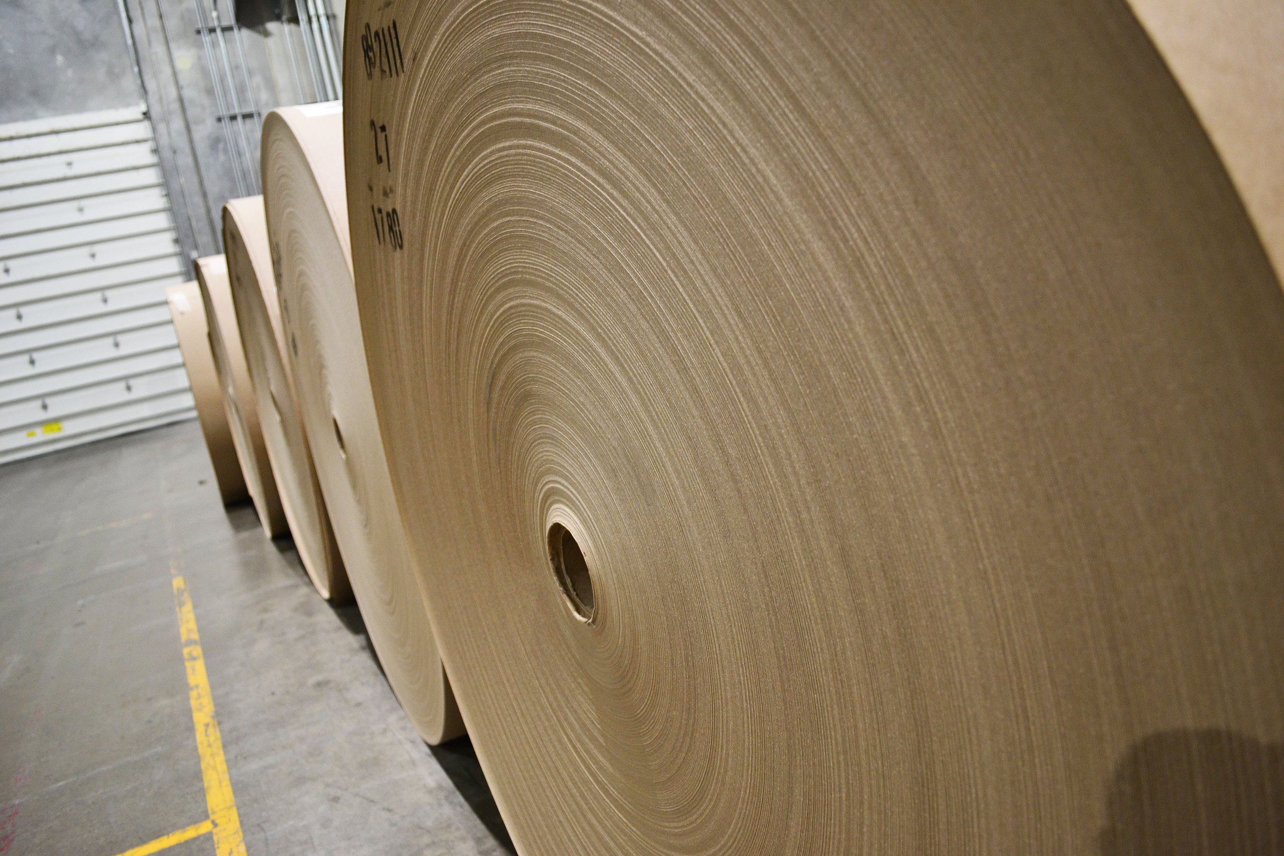 Large rolls of brown corrugated cardboard stacked in an industrial warehouse.