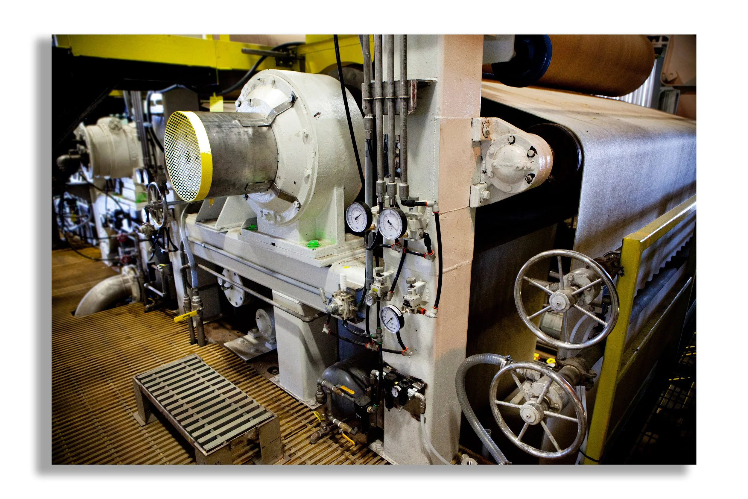Industrial machine with gauges, pipes, and wheels in a factory setting.